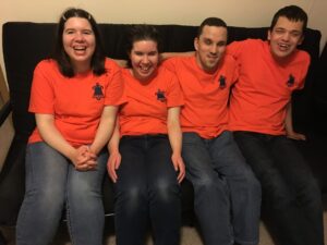 Jessica, Jocelyn, Aedan, and Alex are sitting on a couch. Aedan is smiling and the rest are laughing, looking like they are all having fun.